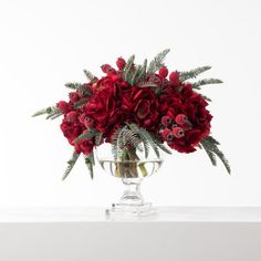 a glass vase filled with red flowers on top of a white table next to a plant