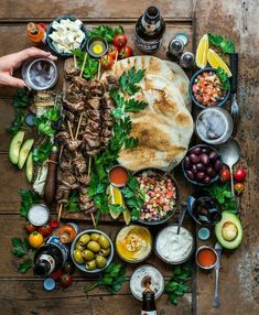 an assortment of food is laid out on a wooden table, including pita bread and olives