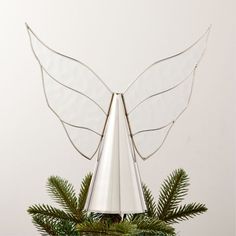 a metal angel decoration on top of a christmas tree with pine branches and evergreen needles