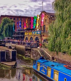 a blue boat traveling down a river next to a tall building with lots of people on it