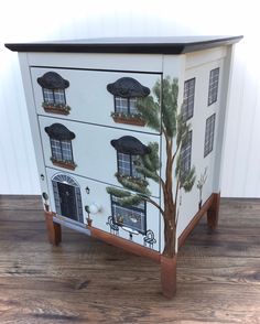 a painted cabinet with windows and trees on the front is sitting on a wooden floor