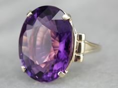 "This is a stunning stone, with a rich color and a sophisticated cut. This natural, well-cut amethyst at the center glimmers with its medium-deep eggplant purple color that flashes with pops of violet and raspberry. We've set this pretty gem into a vintage mounting of yellow gold. Easy to wear, this sits comfortably on the finger and is a nice, bold size that is sure to make a statement! Metal: 14K Yellow Gold Gem: Amethyst 19.50 Carats Gem Measurements: 15.9 x 20.8 mm, Oval Ring Size: 5.50 Mark Oval Stone Ring, Amethyst Cocktail Ring, Right Hand Ring, Right Hand Rings, Eggplant Purple, Hand Ring, Oval Ring, Oval Rings, Amethyst Jewelry