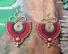 red and gold beaded earrings sitting on top of a wooden table next to green leaves