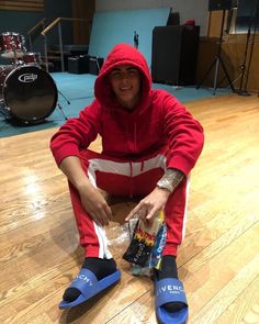 a man in a red hoodie sitting on the floor with his feet propped up