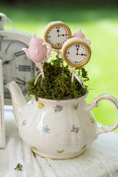 a teapot filled with moss and clocks on top of a table