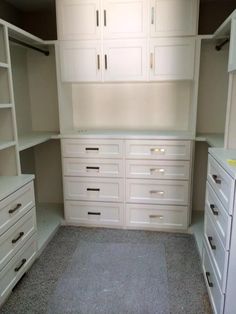 an empty walk in closet with white cabinets and drawers on the wall, carpeted floor