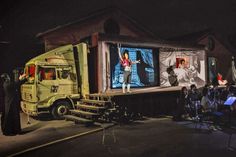 a man standing in front of a large truck at night with people sitting on the side