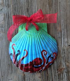 an ornament shaped like a seashell with red ribbon on it sitting on a wooden surface