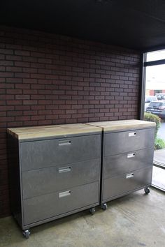 two metal filing cabinets sitting in front of a brick wall next to a large window