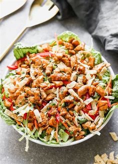 a salad with chicken and lettuce in a white bowl on a gray surface