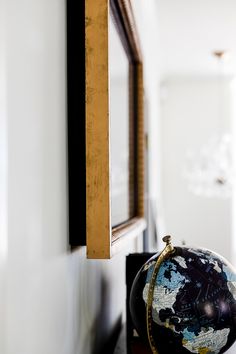 a globe sitting on top of a wooden table next to a mirror and wall hanging