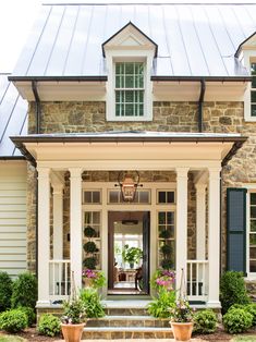 a stone house with green shutters and potted plants on the front steps,