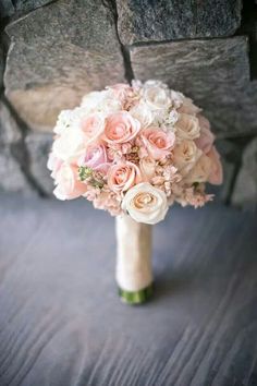 a bridal bouquet sitting on top of a wooden table next to a stone wall