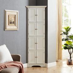 a tall white cabinet in a living room next to a chair and potted plant