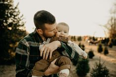 a man holding a baby in his arms while standing next to a christmas tree lot