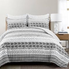 a bed with a black and white patterned comforter on top of it next to a night stand