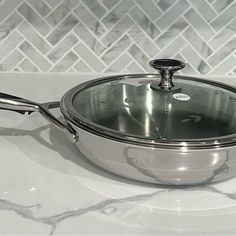 a stainless steel pan with a lid on a marble countertop in front of a white tile backsplash