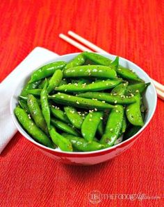 a bowl filled with green beans next to chopsticks on top of a table