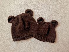 two brown knitted bears hats laying on top of a white bed sheet, one with ears sticking out