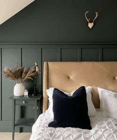 a bed with white sheets and pillows in a room that has green walls, a deer head on the wall