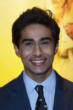 a man in a suit and tie smiling at the camera with a lion behind him