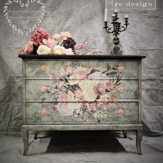 an old dresser with flowers painted on it and a candelabra next to it