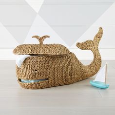 a whale shaped basket sitting on top of a wooden floor next to a toy sailboat