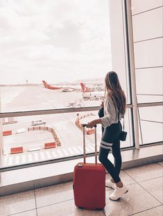 a woman with a red suitcase looking out an airport window