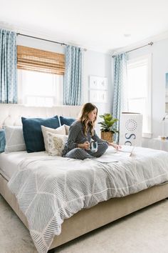 a woman sitting on top of a bed in a room with blue and white curtains