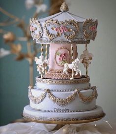 a three tiered carousel cake with pink frosting and gold trimmings on top