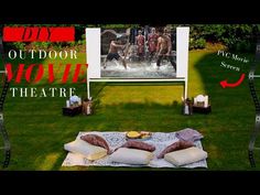 an outdoor movie theater set up in the grass with pillows on it and two chairs