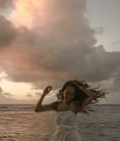 a woman in a white dress standing on the beach with her hair blowing in the wind