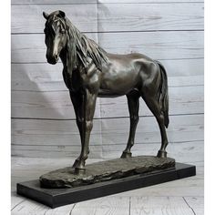 a bronze statue of a horse standing on top of a wooden floor next to a white wall