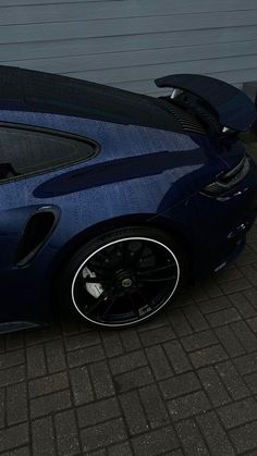 a dark blue sports car parked in front of a garage with its door open and the hood up