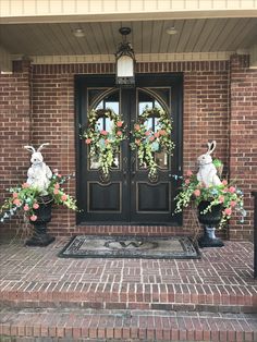 two bunny statues sitting on the front steps of a brick house with wreaths and flowers