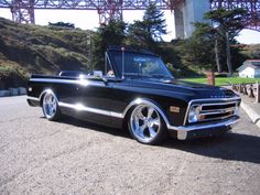 an old black pickup truck parked under a bridge