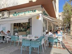 people are sitting at tables outside in front of a restaurant with white awnings