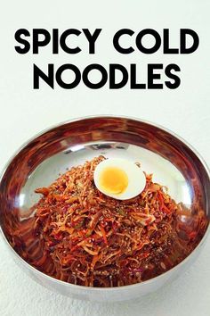 the cover of spicy cold noodles with an egg on top in a silver bowl, against a white background