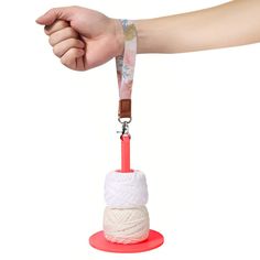 a hand holding a piece of yarn on top of a red object with a brown handle