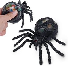 a hand is holding a toy spider and another one has it's eyes open