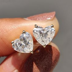 two heart shaped diamond stud earrings on someone's finger