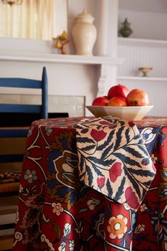 a bowl of apples sitting on top of a table covered in a red and blue cloth