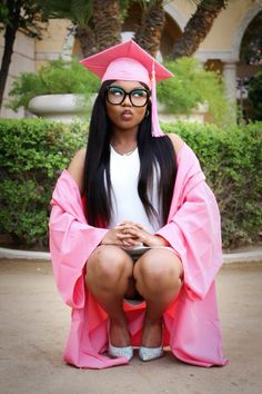 a woman sitting on top of a pink chair wearing glasses and a graduation cap with her legs crossed