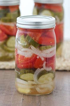 three jars filled with pickles and cucumbers on top of a wooden table