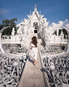 a woman walking down a long walkway in front of a white building with sculptures on it