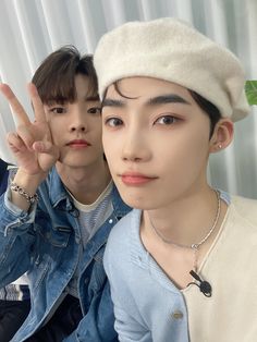 two young men posing for the camera with one holding up his hand and the other wearing a hat