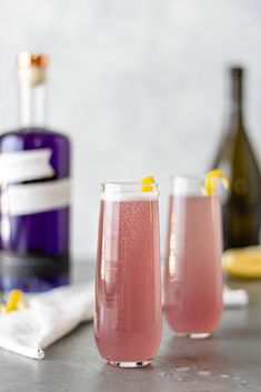 two glasses filled with pink lemonade next to a bottle of booze and a napkin