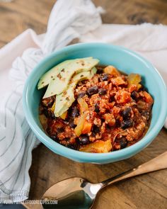 a blue bowl filled with chili and avocado on top of a wooden table