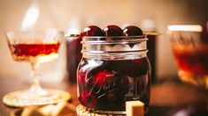 a jar filled with cherries sitting on top of a table next to a glass of wine