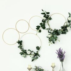 three circular wreaths with flowers and greenery hanging on the wall next to candles